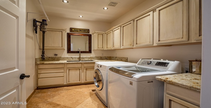 Large functional laundry with deep stainless steel sink and granite slab countertops.