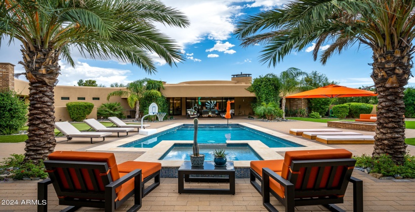 STUNNING Resort-Like Backyard featuring covered patio with outdoor furniture, BBQ grill, sparkling blue pool and spa, sun loungers, firepit, putting green, and ample yard space.