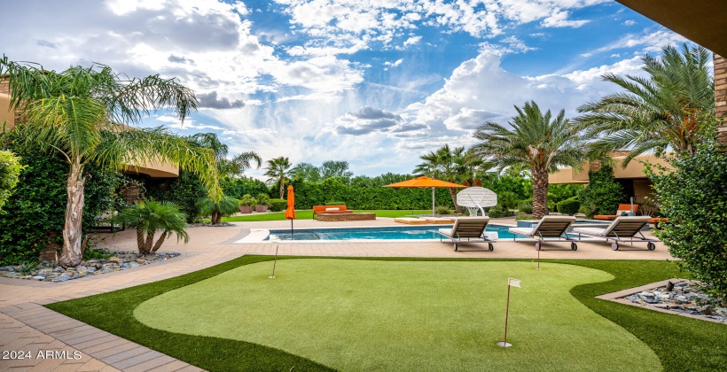 STUNNING Resort-Like Backyard featuring covered patio with outdoor furniture, BBQ grill, sparkling blue pool and spa, sun loungers, firepit, putting green, and ample yard space.