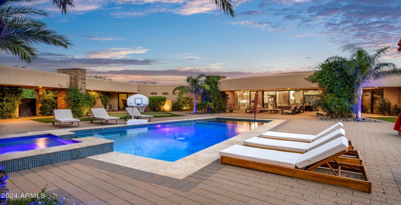 STUNNING Resort-Like Backyard featuring covered patio with outdoor furniture, BBQ grill, sparkling blue pool and spa, sun loungers, firepit, putting green, and ample yard space.