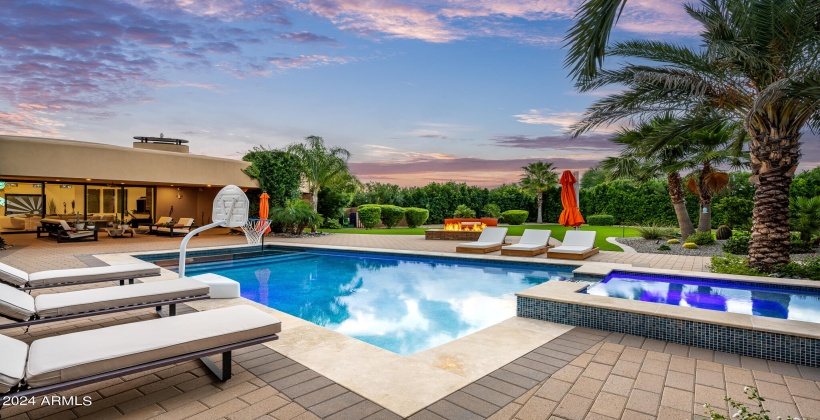 STUNNING Resort-Like Backyard featuring covered patio with outdoor furniture, BBQ grill, sparkling blue pool and spa, sun loungers, firepit, putting green, and ample yard space.