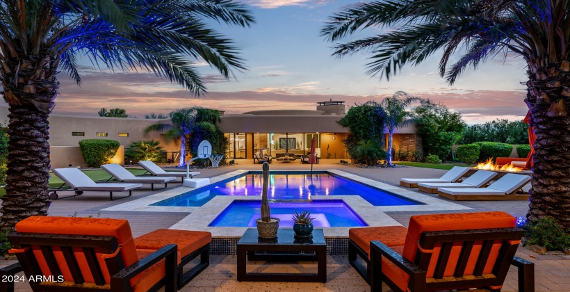 STUNNING Resort-Like Backyard featuring covered patio with outdoor furniture, BBQ grill, sparkling blue pool and spa, sun loungers, firepit, putting green, and ample yard space.