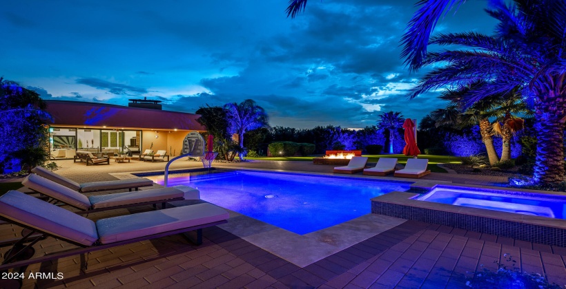 STUNNING Resort-Like Backyard featuring covered patio with outdoor furniture, BBQ grill, sparkling blue pool and spa, sun loungers, firepit, putting green, and ample yard space.